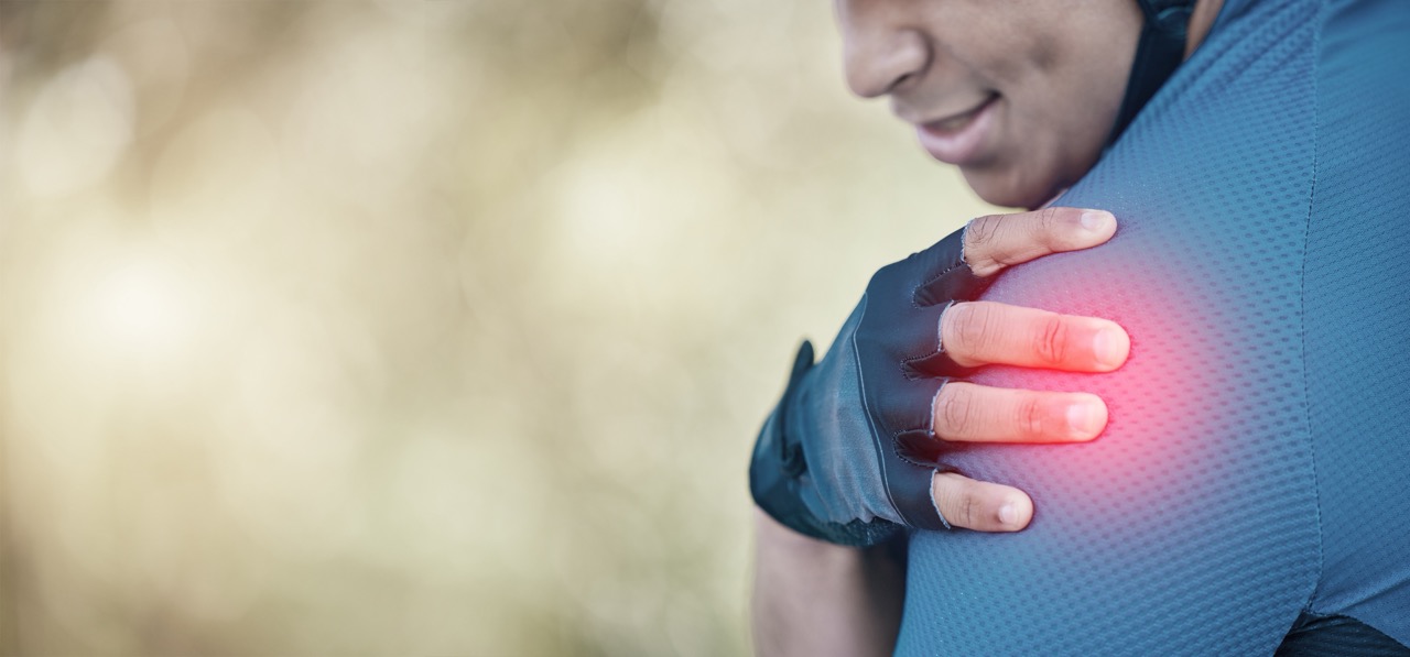 A male bicyclist’s left shoulder highlighted in red for pain, with his gloved hand holding onto his shoulder.
