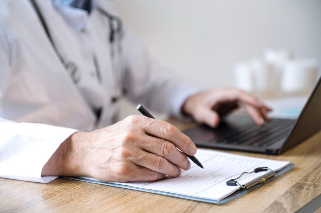 selective focus on doctor hand with pen filling patient medical chart at appointment in clinic. cropped shot of physician write treatment plan at paper form. diagnosis, medical conclusion concept
