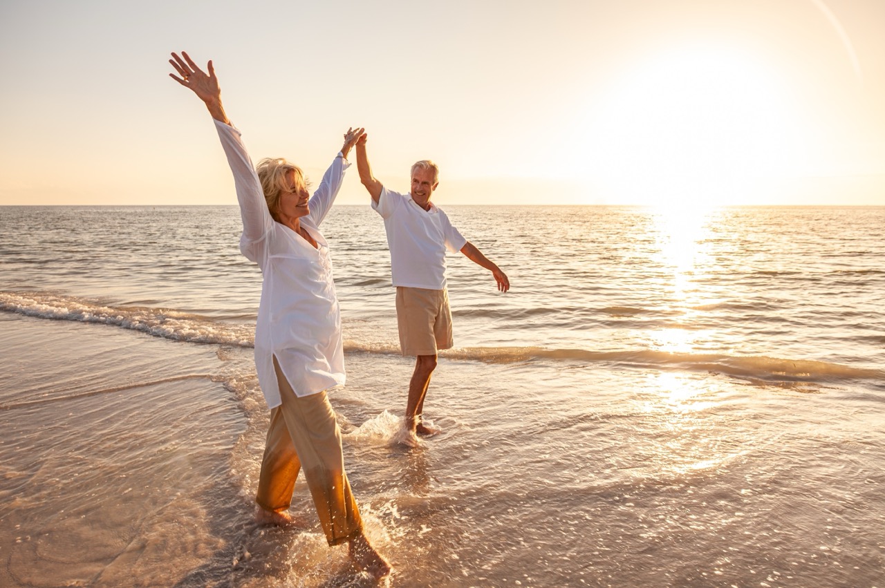 A couple walking on the beach with their hands in the air.
