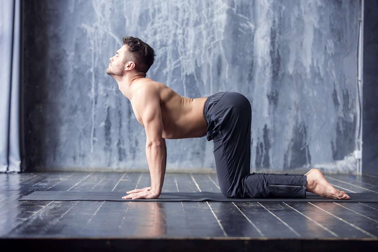 Yoga. Young yogi men practices yoga asana bitilasana - cow pose or cat-cow pose in urban studio. Yoga men workout on black mat.
