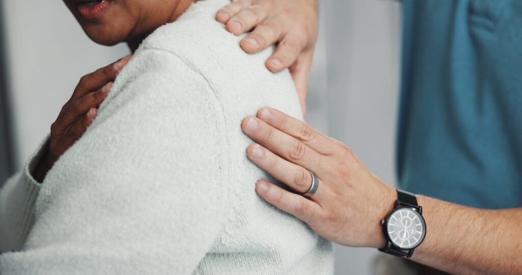 A shoulder orthopedist uses both hands to examine a female patient’s left shoulder.