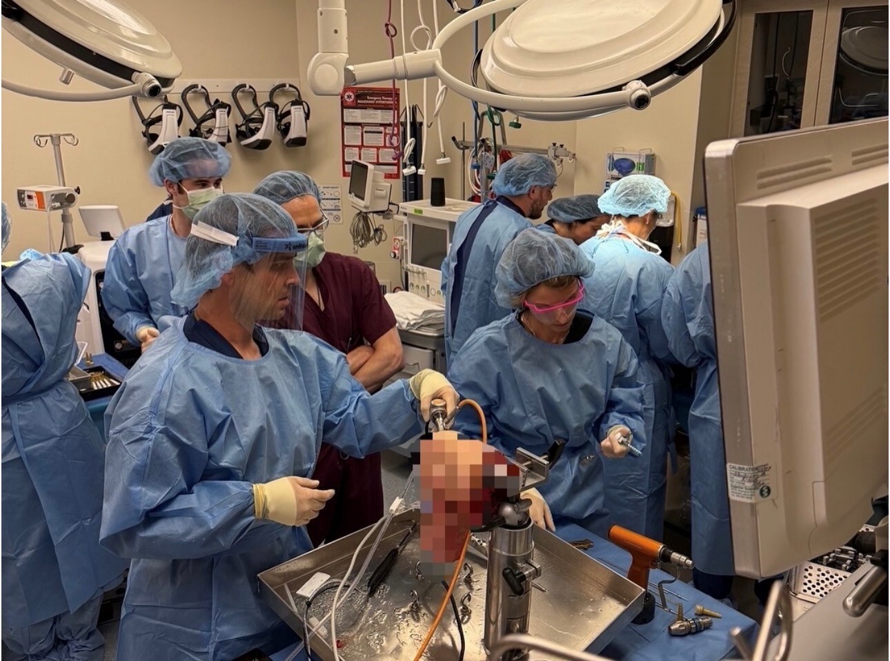 A few SCOI doctors wearing scrubs and protective gear participate in a hands-on surgical training session in a teaching lab.